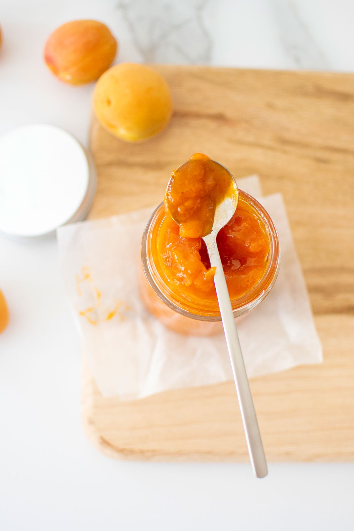 organic apricot jam in a glass jar on a wood cutting board on a marble counter.