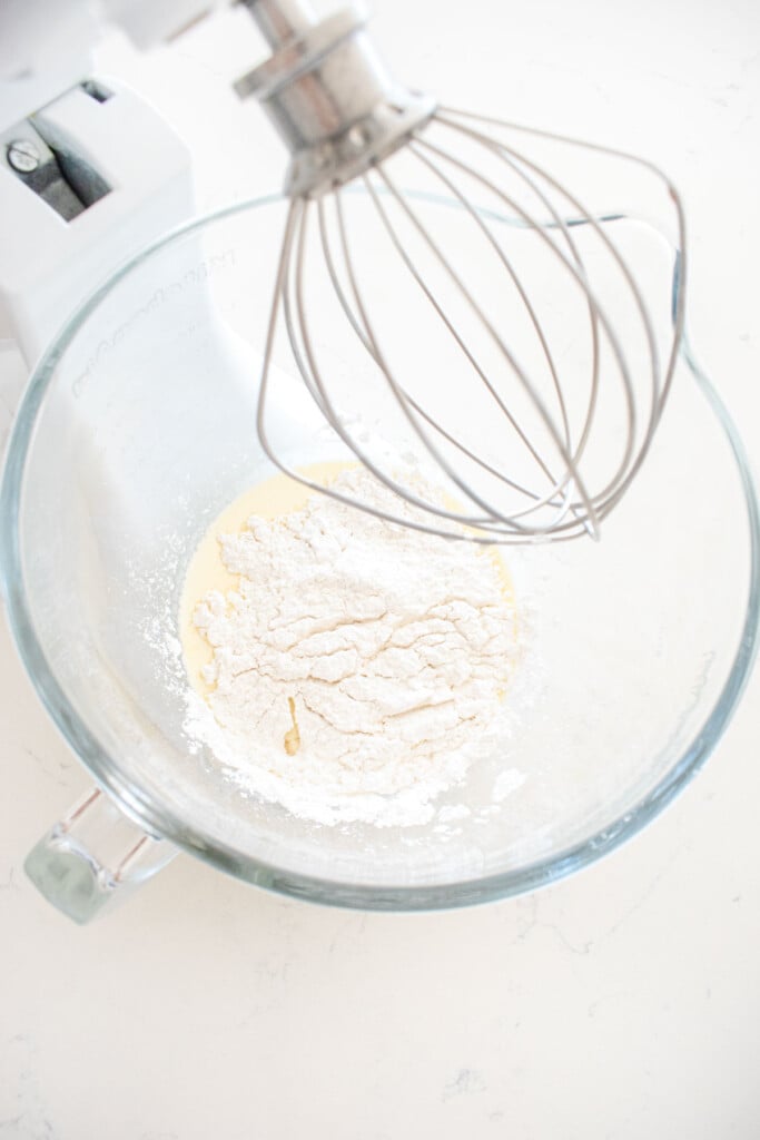 ingredients for cherry whipped cream frosting in a glass stand mixing bowl on a white marble counter.