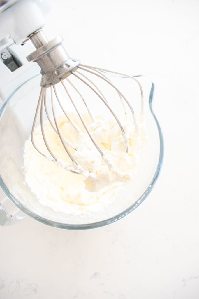 cherry whipped cream frosting in a glass stand mixing bowl on a white marble counter.
