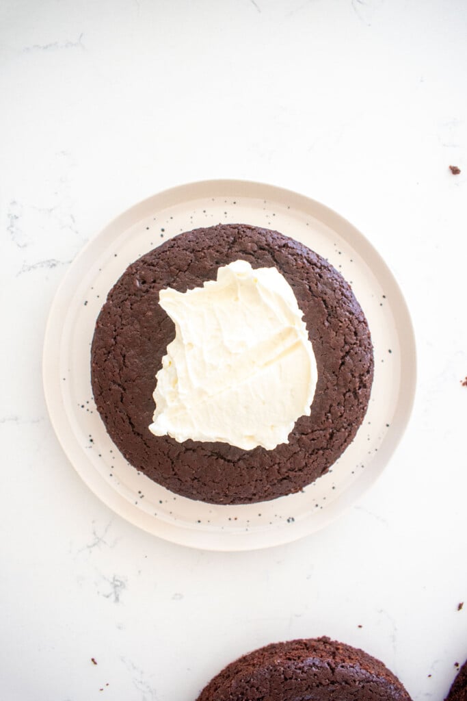 chocolate cherry whipped cream cake being assembled on a white marble counter.