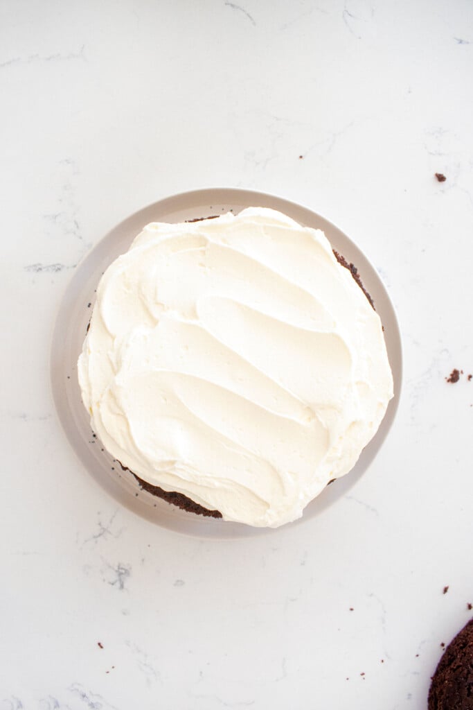 chocolate cherry whipped cream cake being assembled on a white marble counter.
