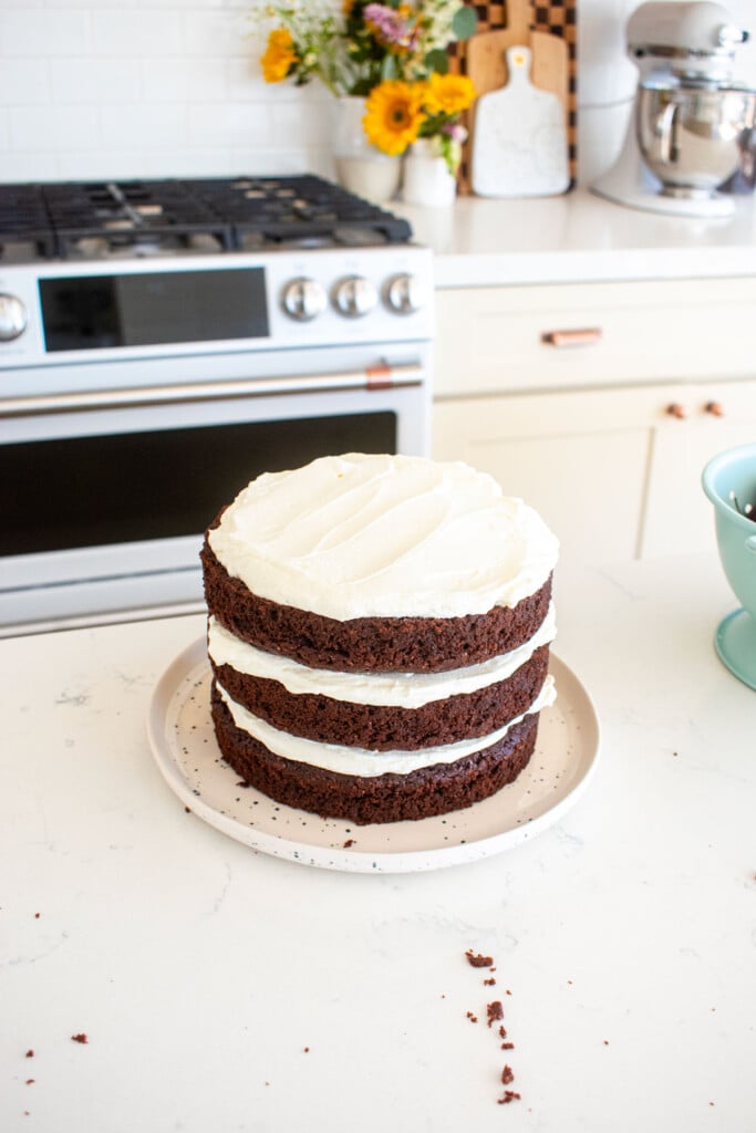 chocolate cherry whipped cream cake being assembled on a white marble counter.