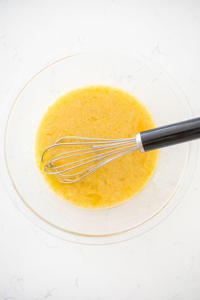 wet ingredients mixed together with a whisk for chocolate cake in a glass mixing bowl on a white marble counter.