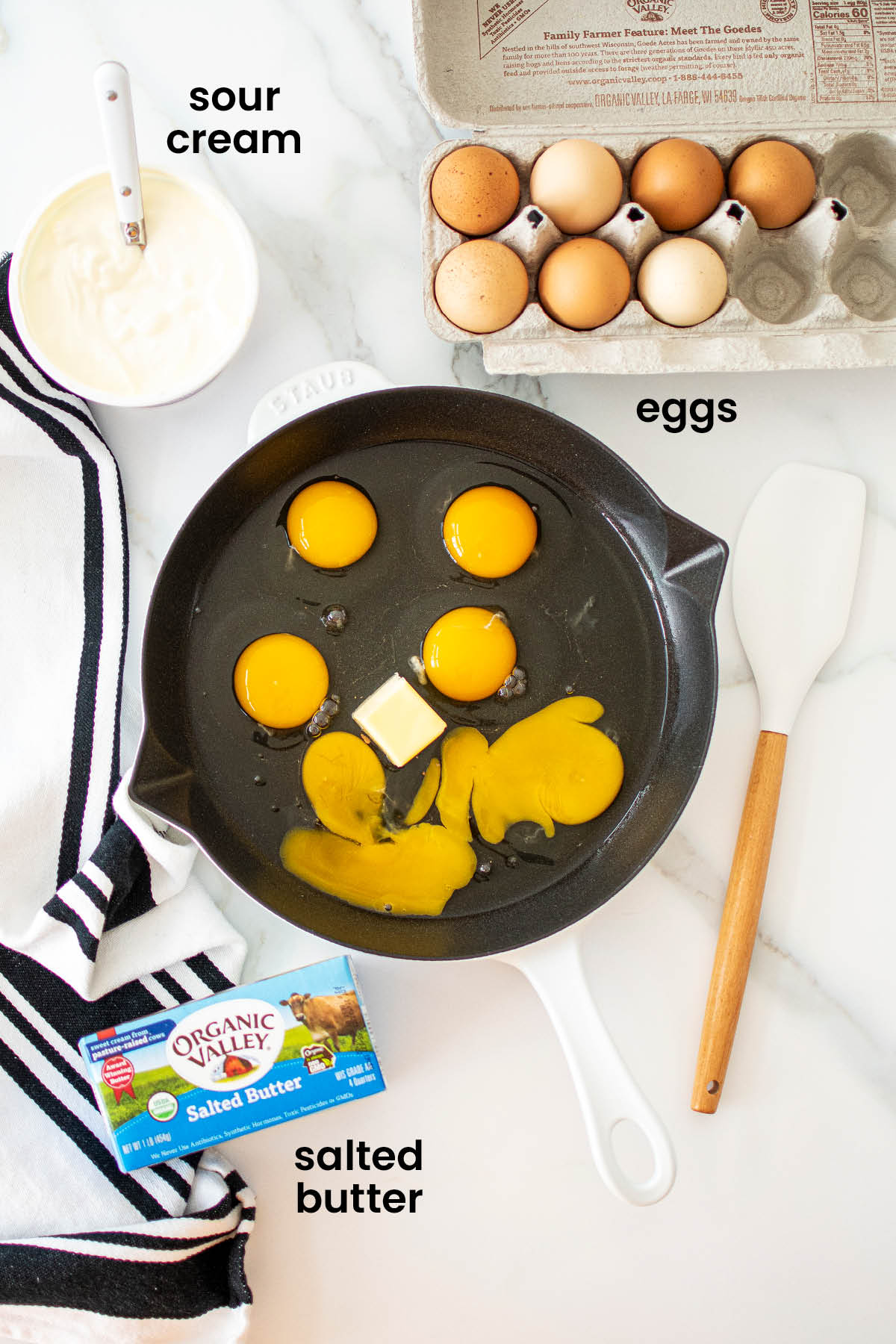 individual ingredients for fluffy scrambled eggs with sour cream laid out against a white background.