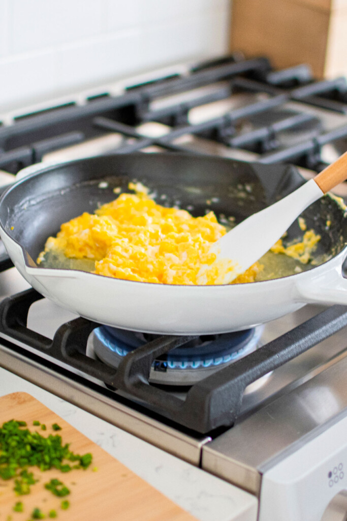 scrambled eggs being stirred in a cast iron skillet on the stovetop.
