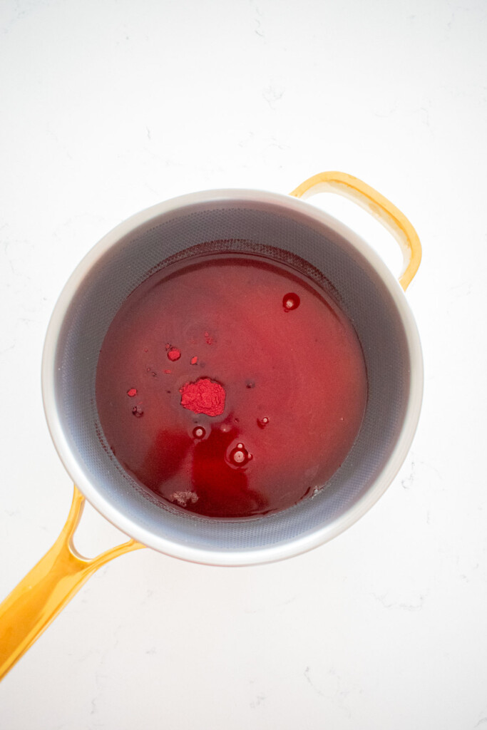 ingredients for homemade cherry marshmallows in a stainless steel pot on a white marble counter.