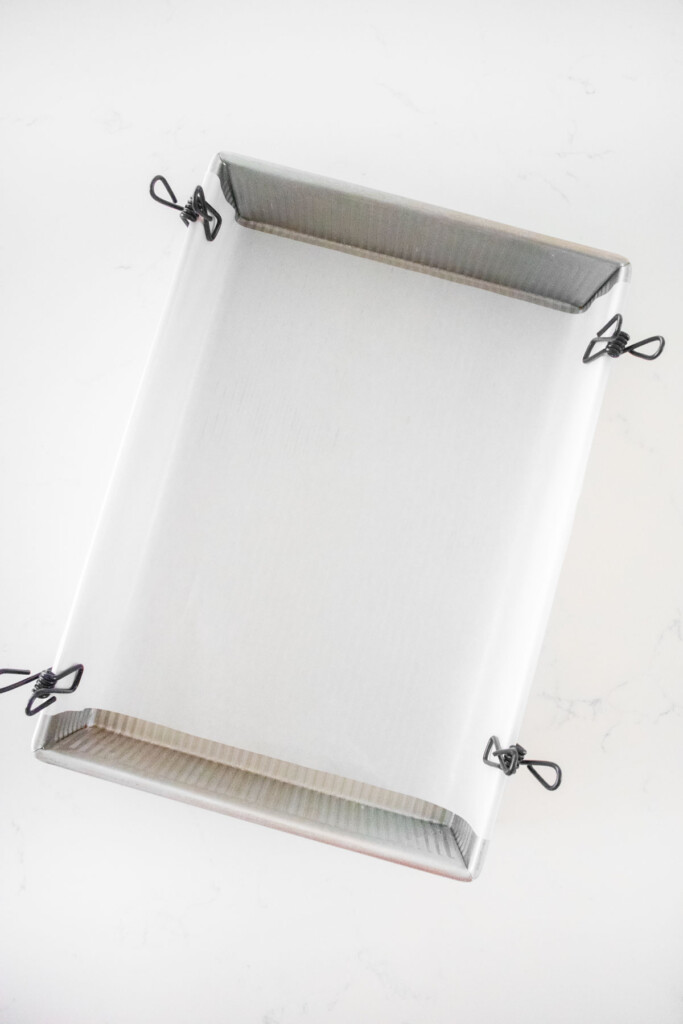 parchment paper in a baking pan held up with binder clips on a white marble counter.