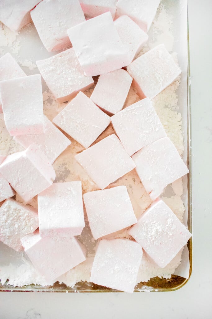 homemade cherry marshmallows cut into large marshmallow squares on a baking sheet on a white marble counter.