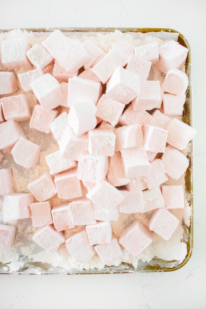 homemade cherry marshmallows cut into mini marshmallow squares on a baking sheet on a white marble counter.
