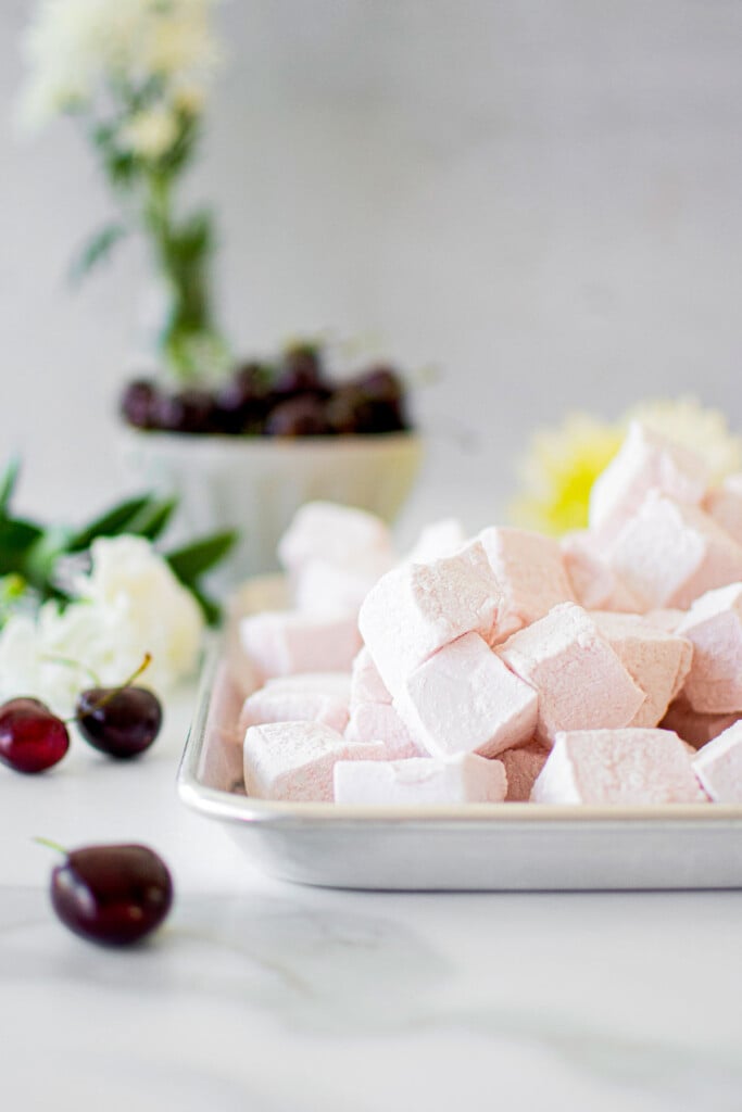 homemade cherry marshmallows on a baking sheet on a marble counter.