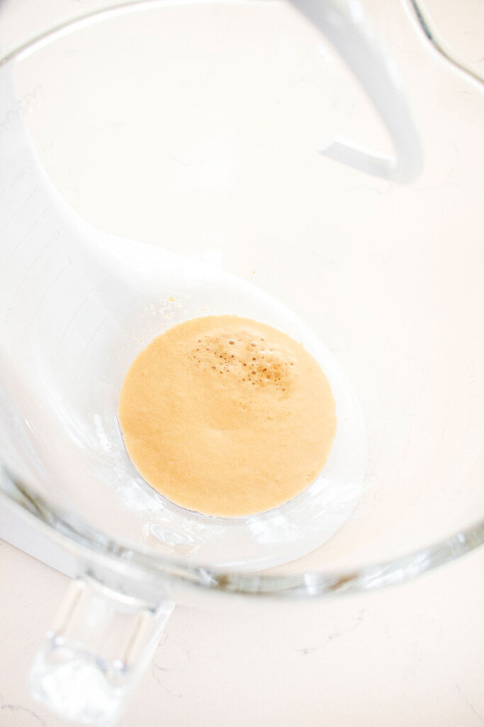 yeast and water in a glass mixing bowl on a white marble counter.