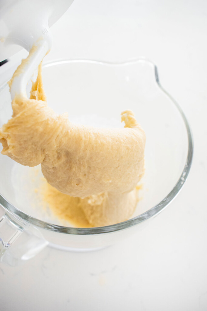 one rise cinnamon dough being mixed with a dough hook in a stand mixer on a white marble counter.