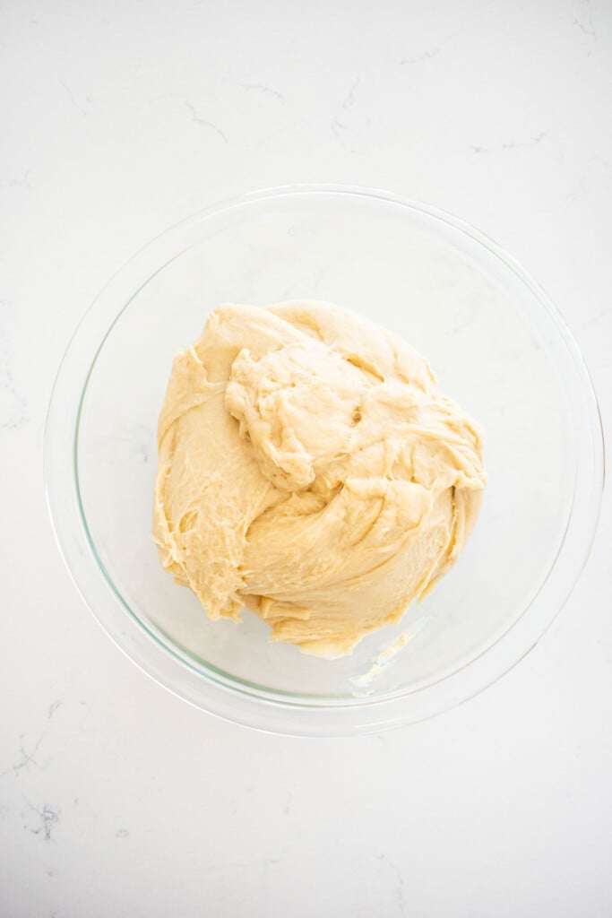 one rise cinnamon roll dough in a glass mixing bowl on a white marble counter.
