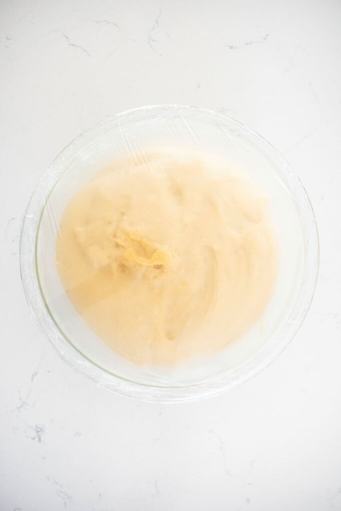 one rise cinnamon roll dough in a glass mixing bowl on a white marble counter.
