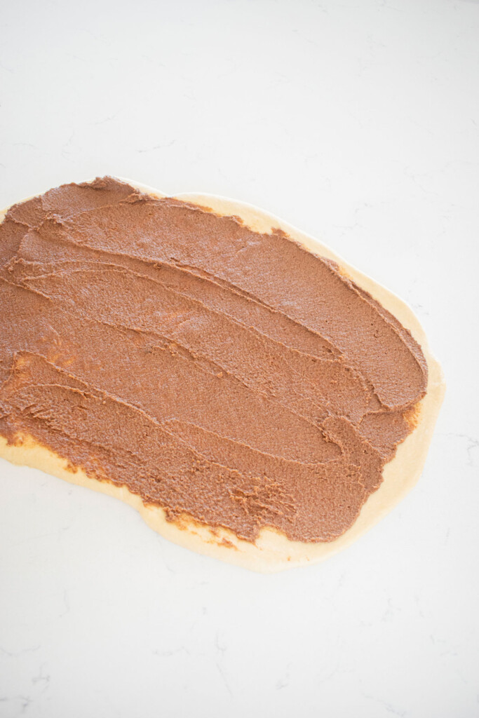 cinnamon roll dough rolled out and spread with filling on a white marble counter.