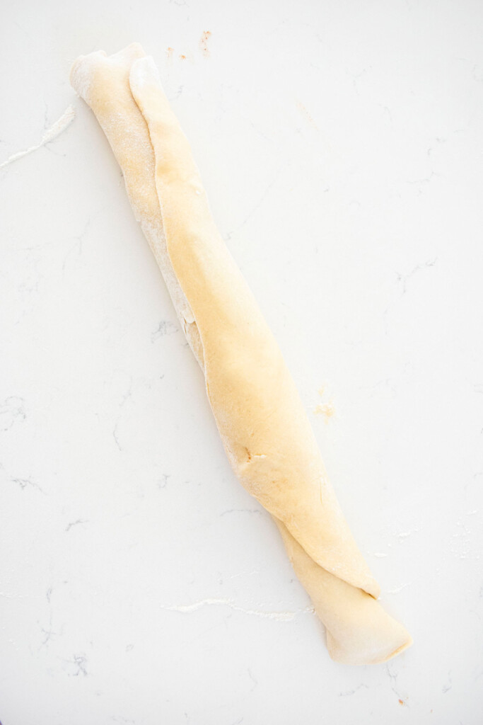 cinnamon roll dough rolled into a log on a white marble counter.