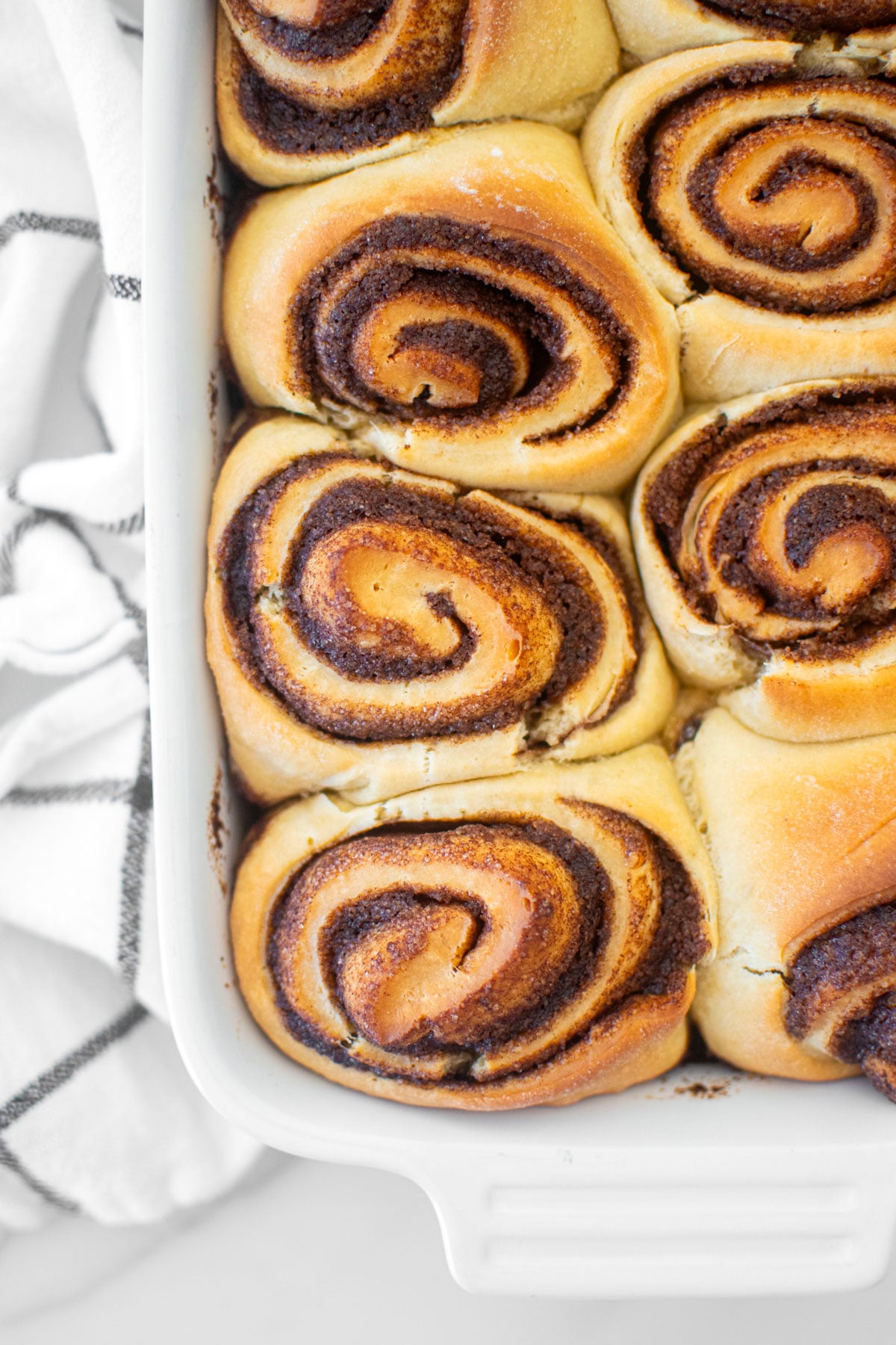 golden brown homemade cinnamon rolls in a white baking dish on a white marble counter.