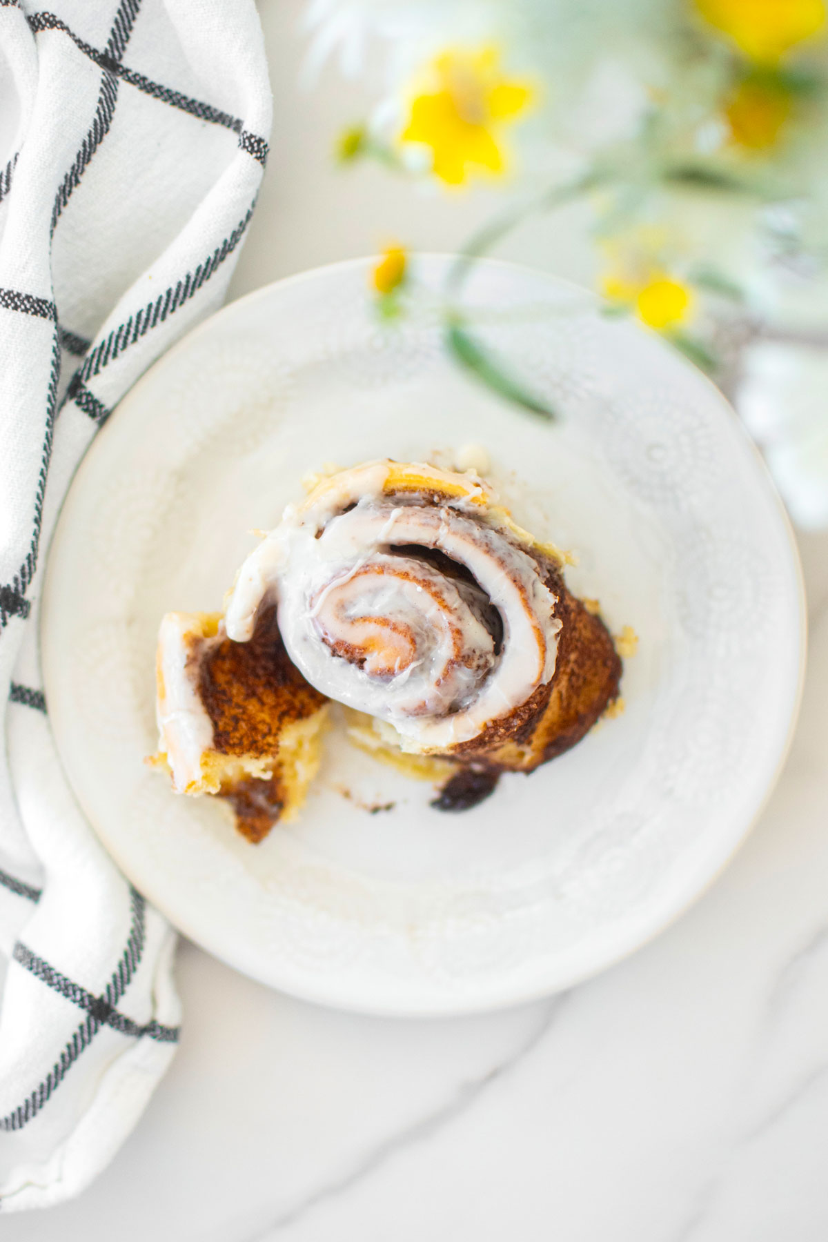 homemade cinnamon roll on a white plate on marble countertop with fresh flowers.