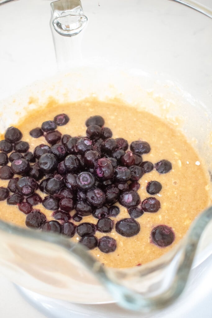 blueberries added into banana bread batter in a glass mixing bowl.
