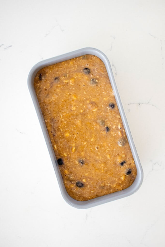 blueberry buttermilk banana bread batter in a loaf pan on a white marble counter.