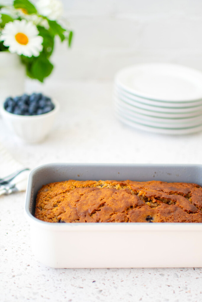 blueberry buttermilk banana bread in a loaf pan on a white stone counter.