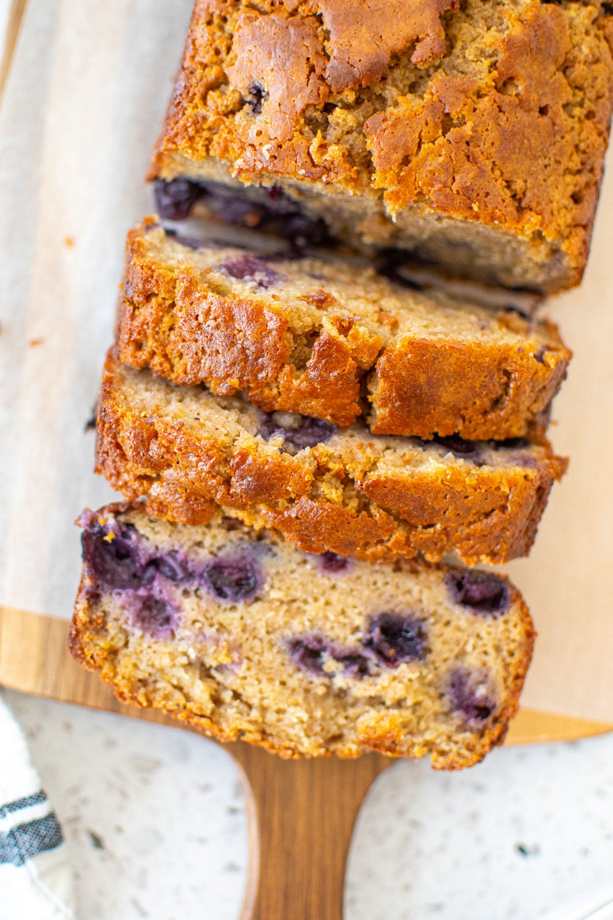 blueberry buttermilk banana bread sliced on a wood cutting board.