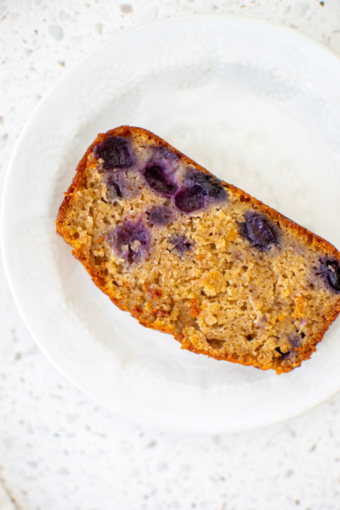 slice of blueberry buttermilk banana bread on a white plate.