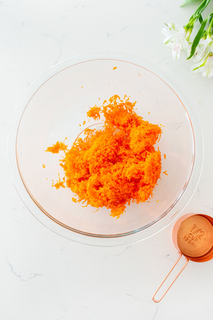 glass mixing bowl on a white marble counter with grated carrots.