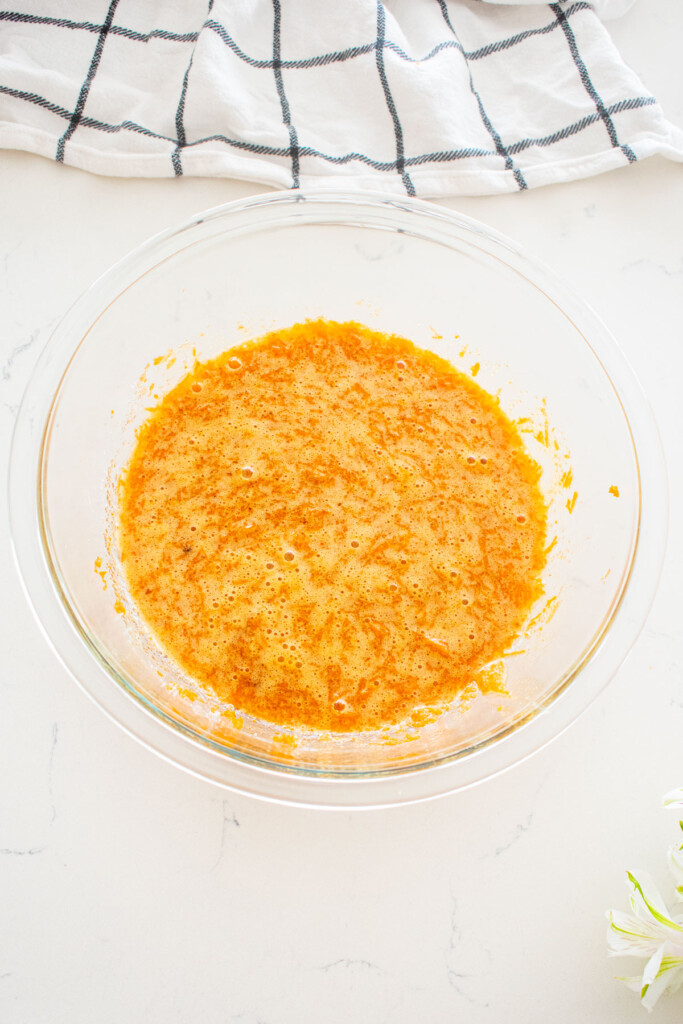 wet ingredients mixed together for brown sugar carrot cupcakes in a glass mixing bowl on a white marble counter.