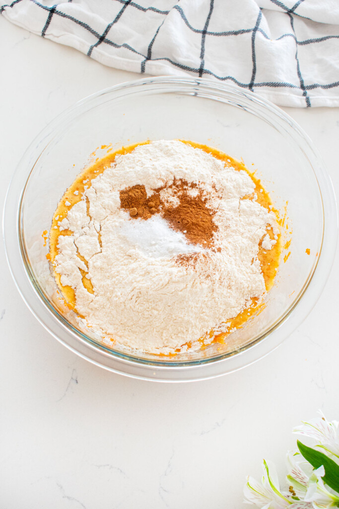all ingredients for brown sugar carrot cupcakes in a glass mixing bowl on a white marble counter.