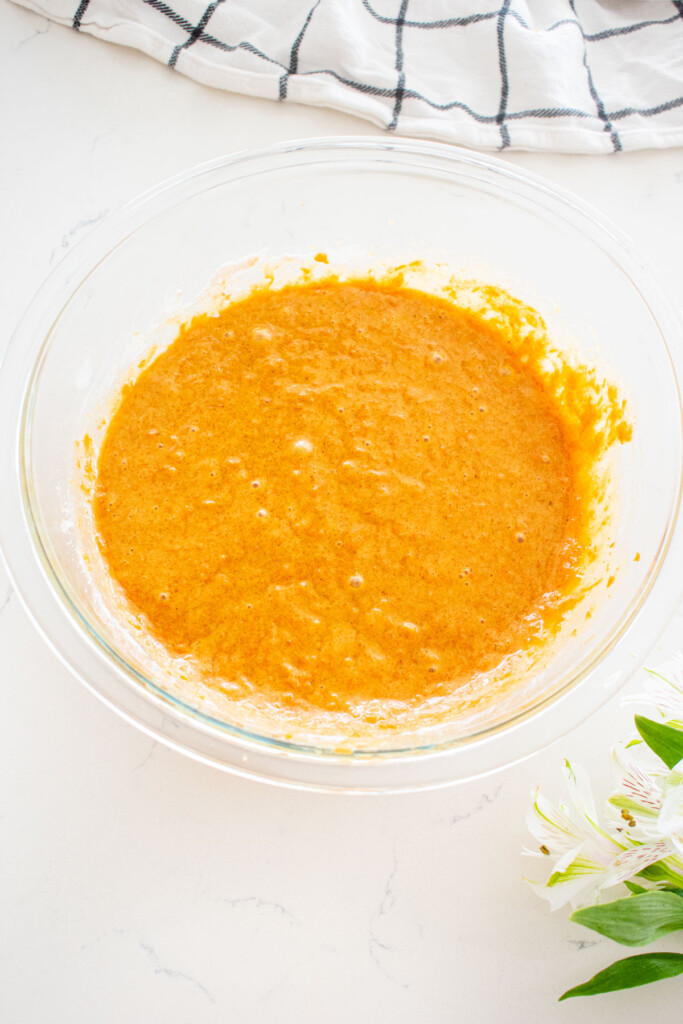 brown sugar carrot cupcake batter in a glass mixing bowl on a white marble counter.