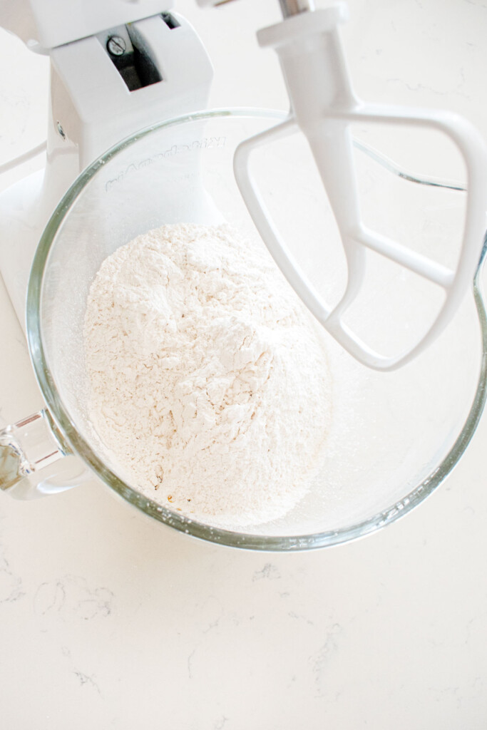 ingredients for cream cheese frosting in a glass stand mixing bowl on a white marble counter.