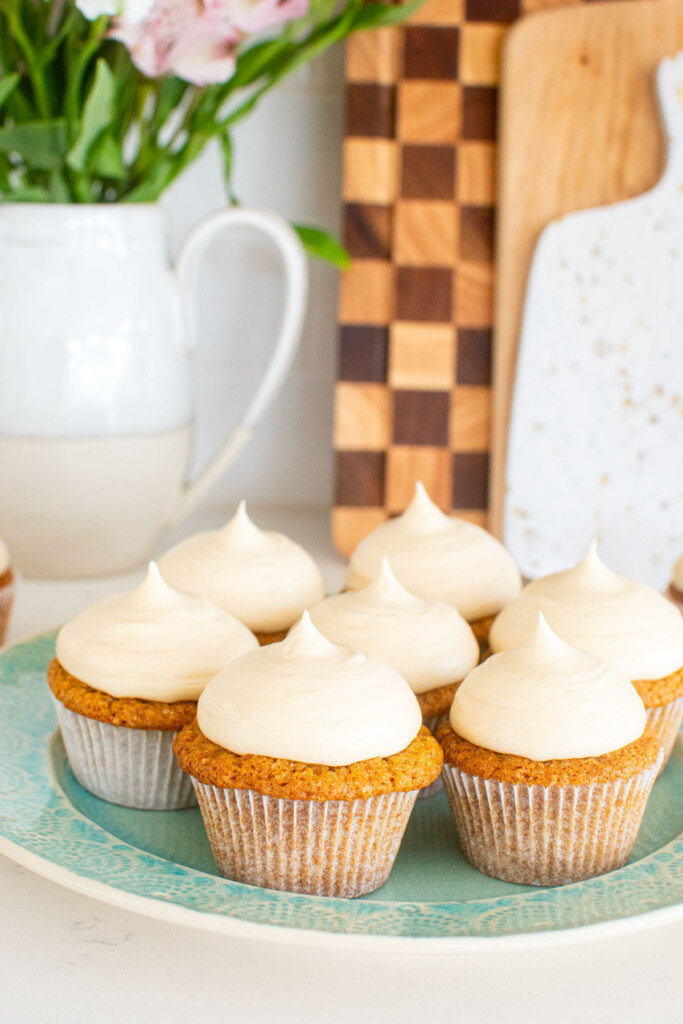 brown sugar carrot cupcakes on a green plate on a white marble counter with a vase of flowers.