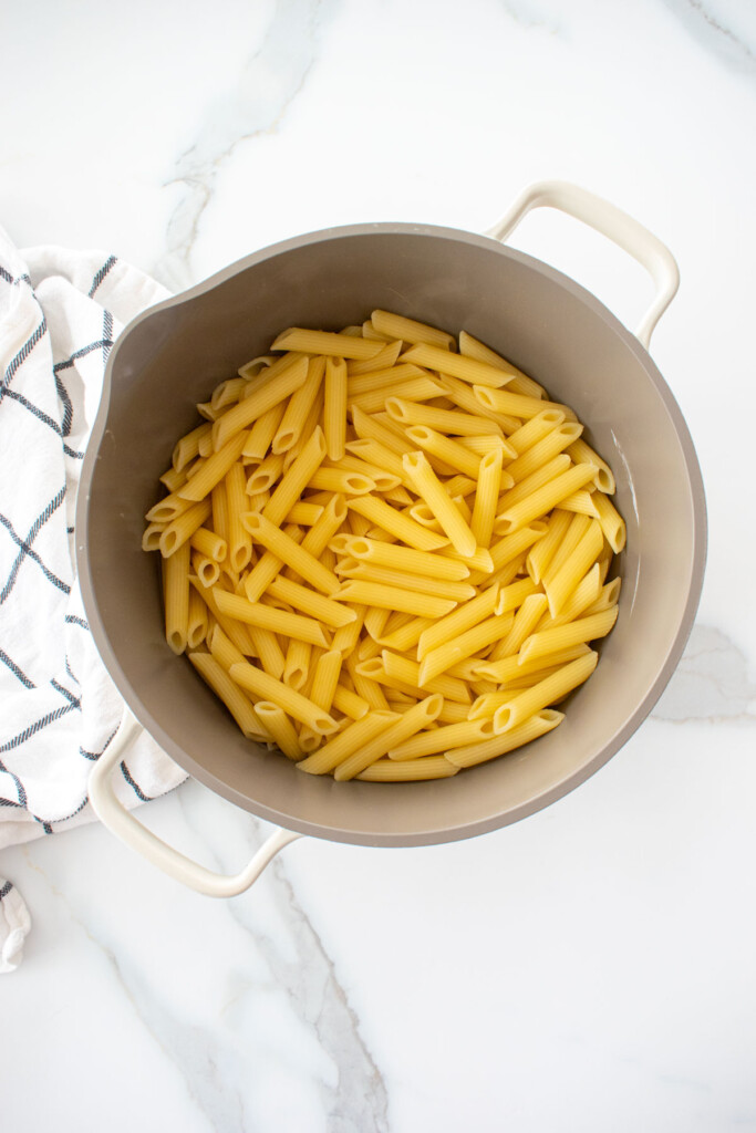 cooked penne noodles in a pot on a white marble counter.