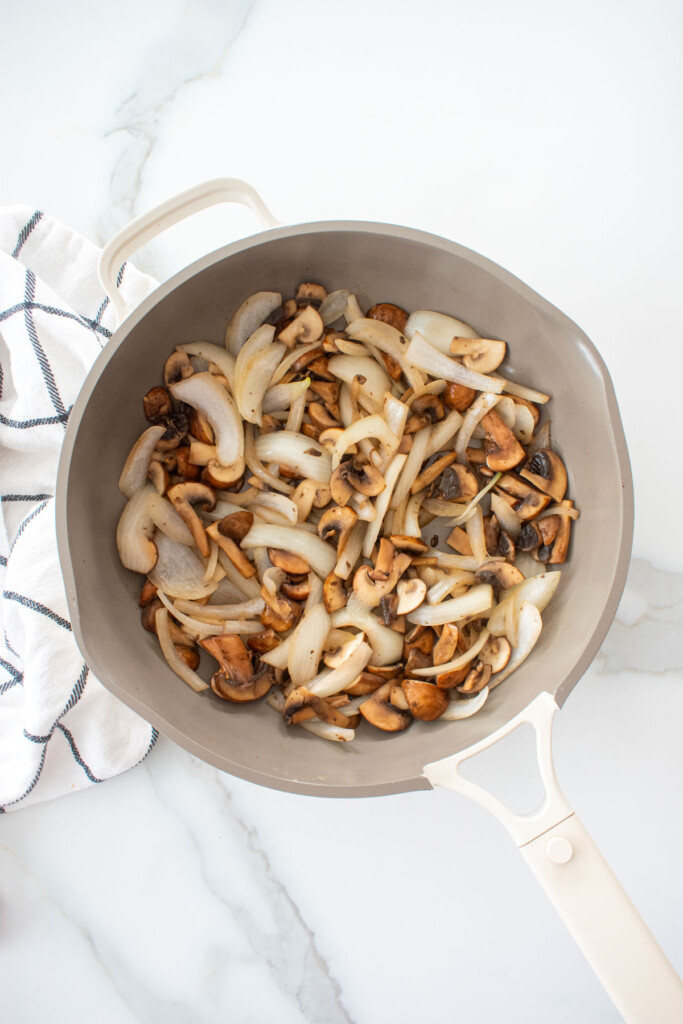 sauted onions and mushrooms in a large skillet on a white marble counter.