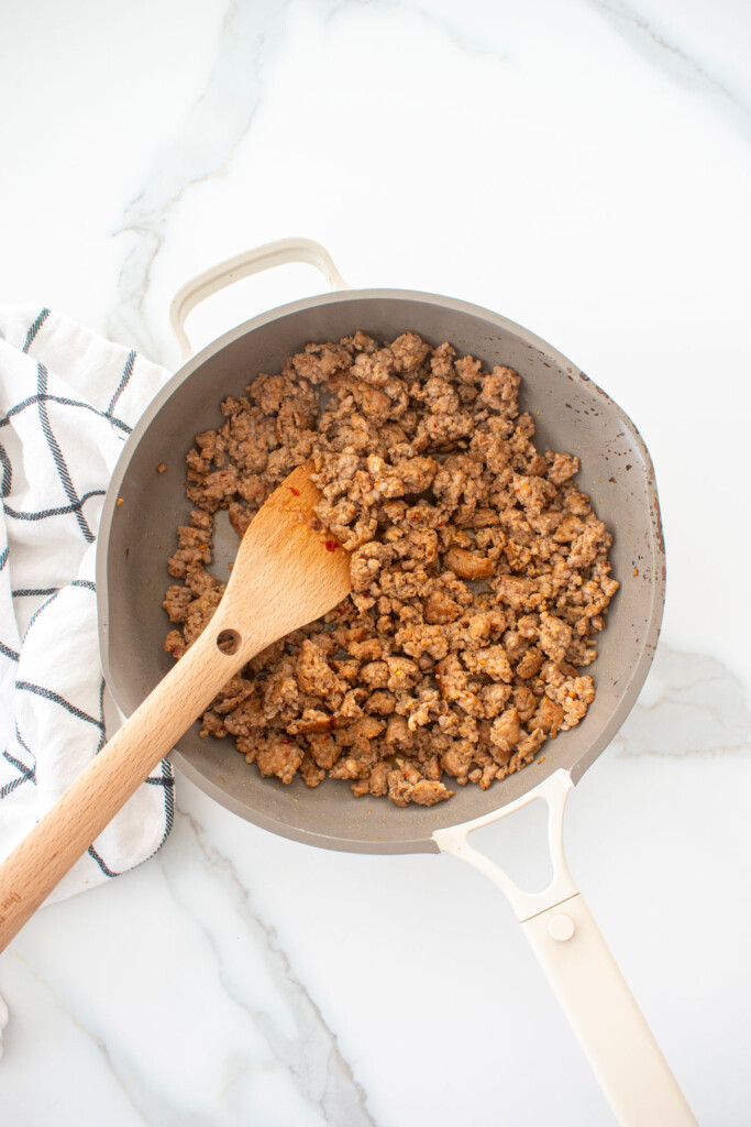 cooked Italian sausage in a large skillet on a white marble counter.