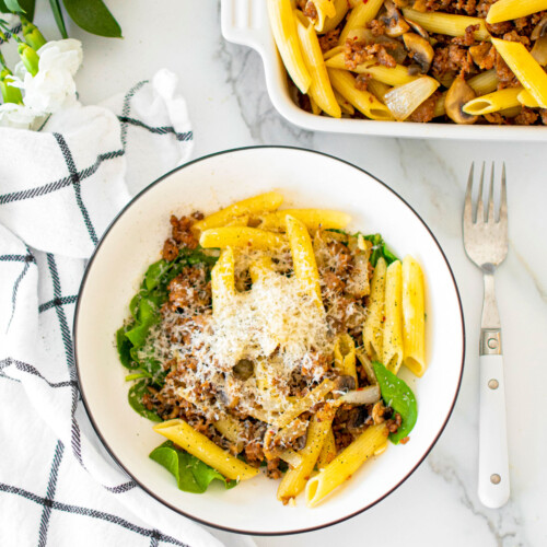 butter parmesan pasta with italian sausage in a bowl on a white marble countertop.