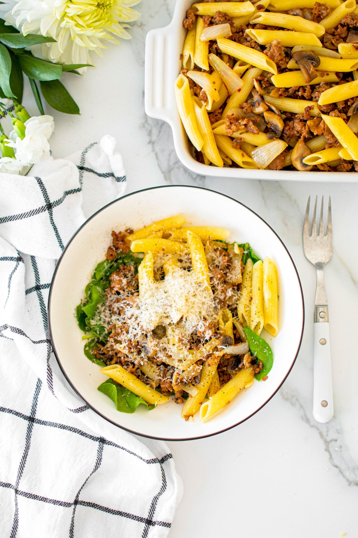 butter parmesan pasta with italian sausage in a bowl on a white marble countertop.