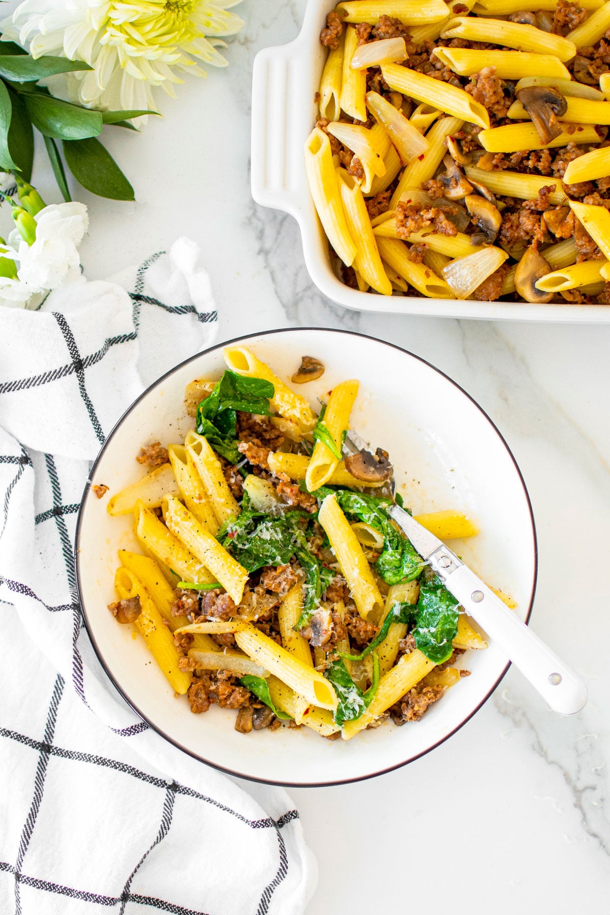 butter parmesan pasta with italian sausage in a bowl on a white marble countertop.