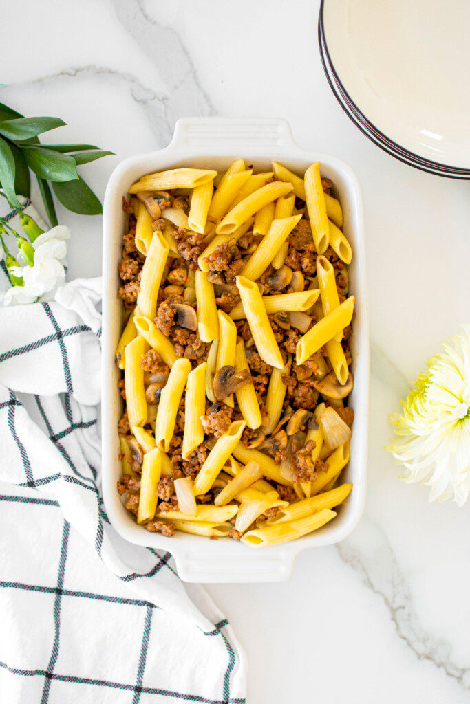 pasta and italian sausage in a white baking dish on a marble countertop.