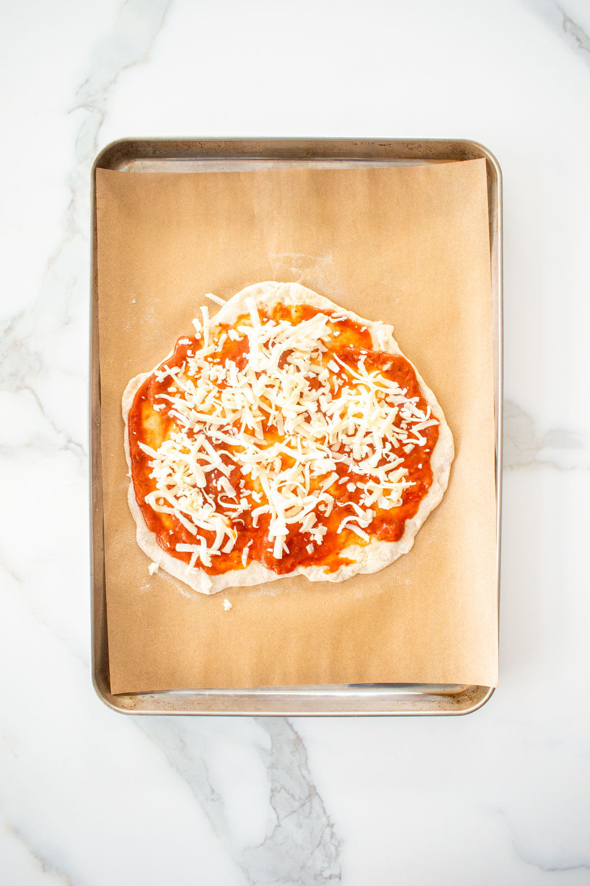 chicago style thin crust pizza dough with toppings on a baking sheet on a white marblec ounter.
