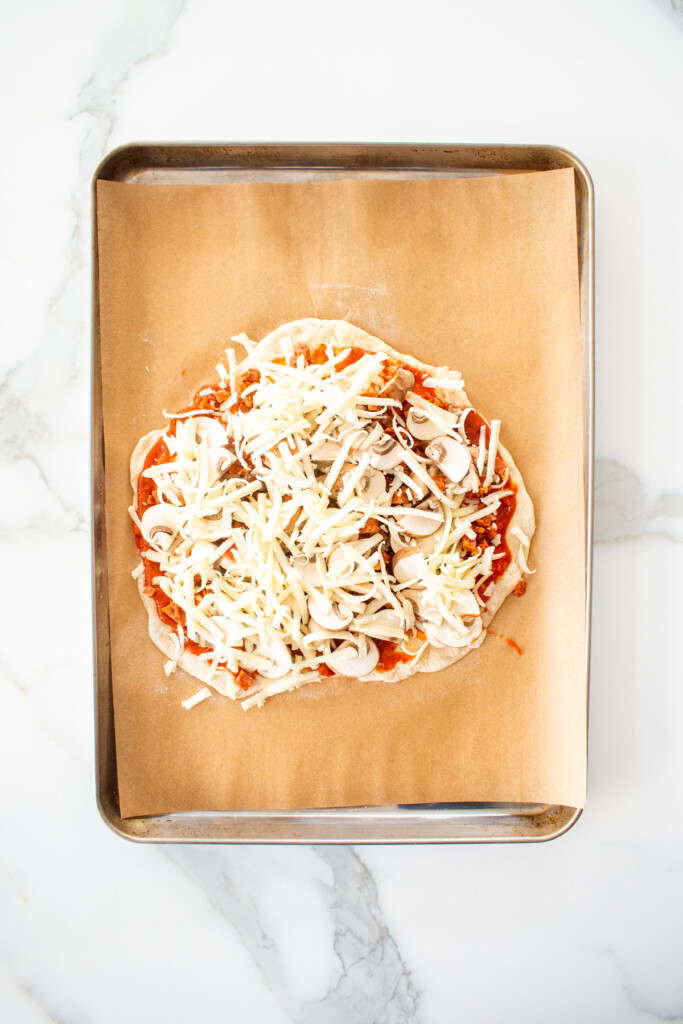 chicago style thin crust pizza dough with toppings on a baking sheet on a white marblec ounter.