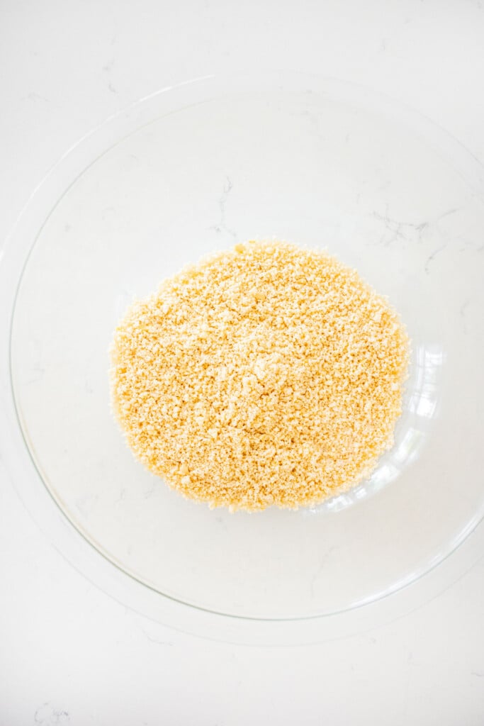 glass bowl of ground up almonds on a white marble counter.