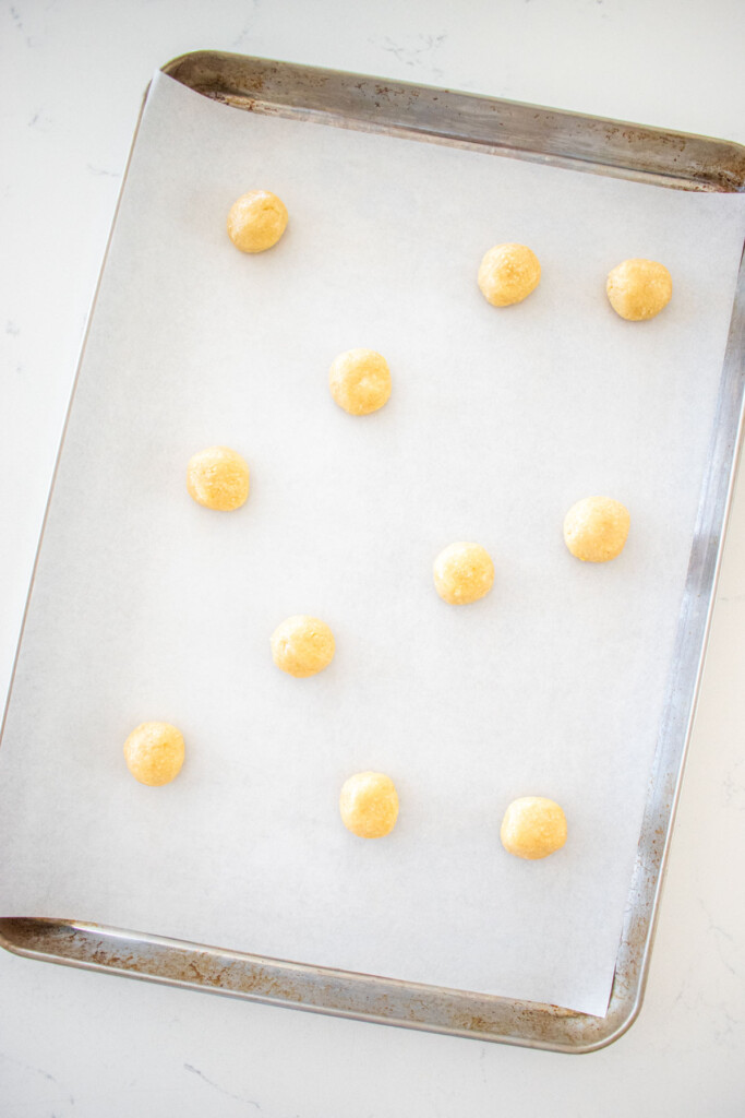 florentine cookie dough balls on a baking sheet with parchment paper on a marble counter.
