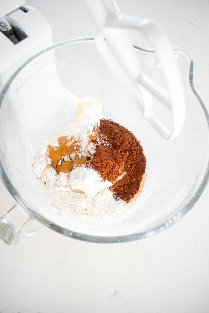 butter, powdered sugar, peanut butter and cocoa powder in a glass mixing bowl on a marble counter.