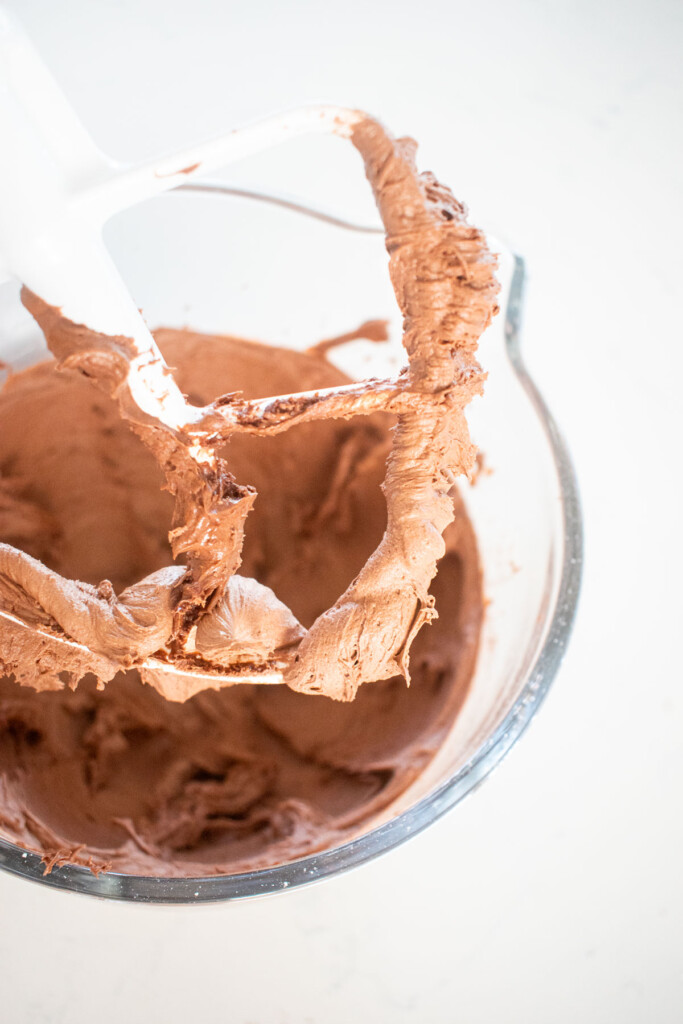 chocolate peanut butter buttercream in a glass mixing bowl on a marble counter.