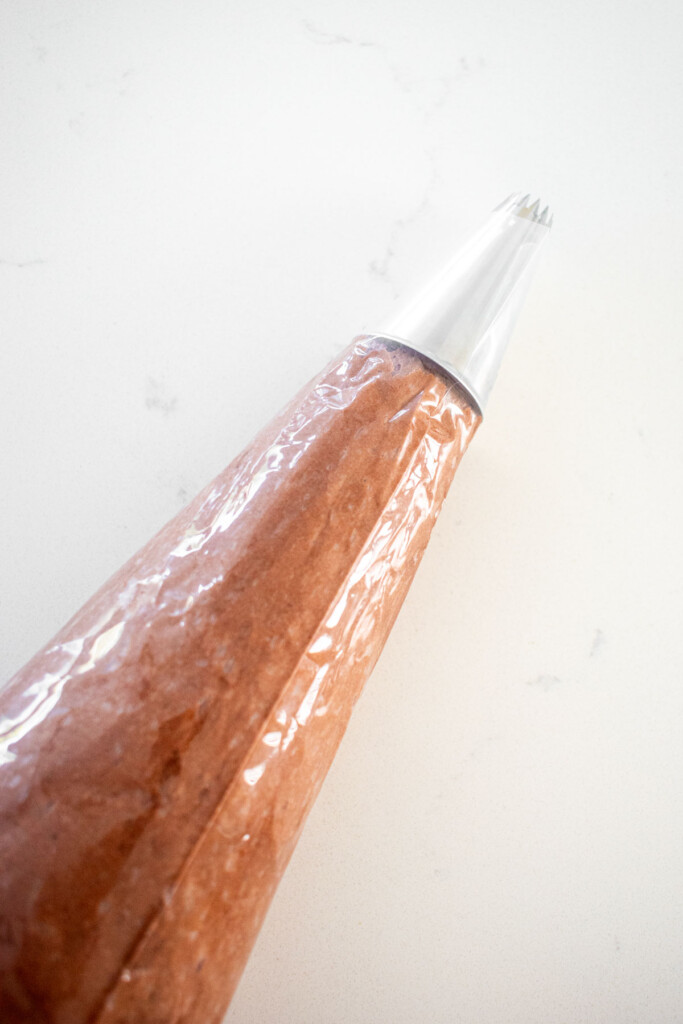 piping bag with a star decorating tip with chocolate peanut butter frosting on a marble counter.