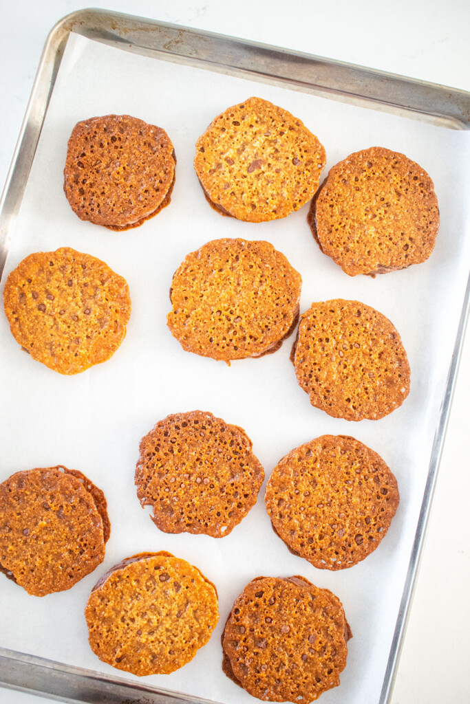 chocolate peanut butter florentine sandwich cookies on a baking sheet on a marble counter.