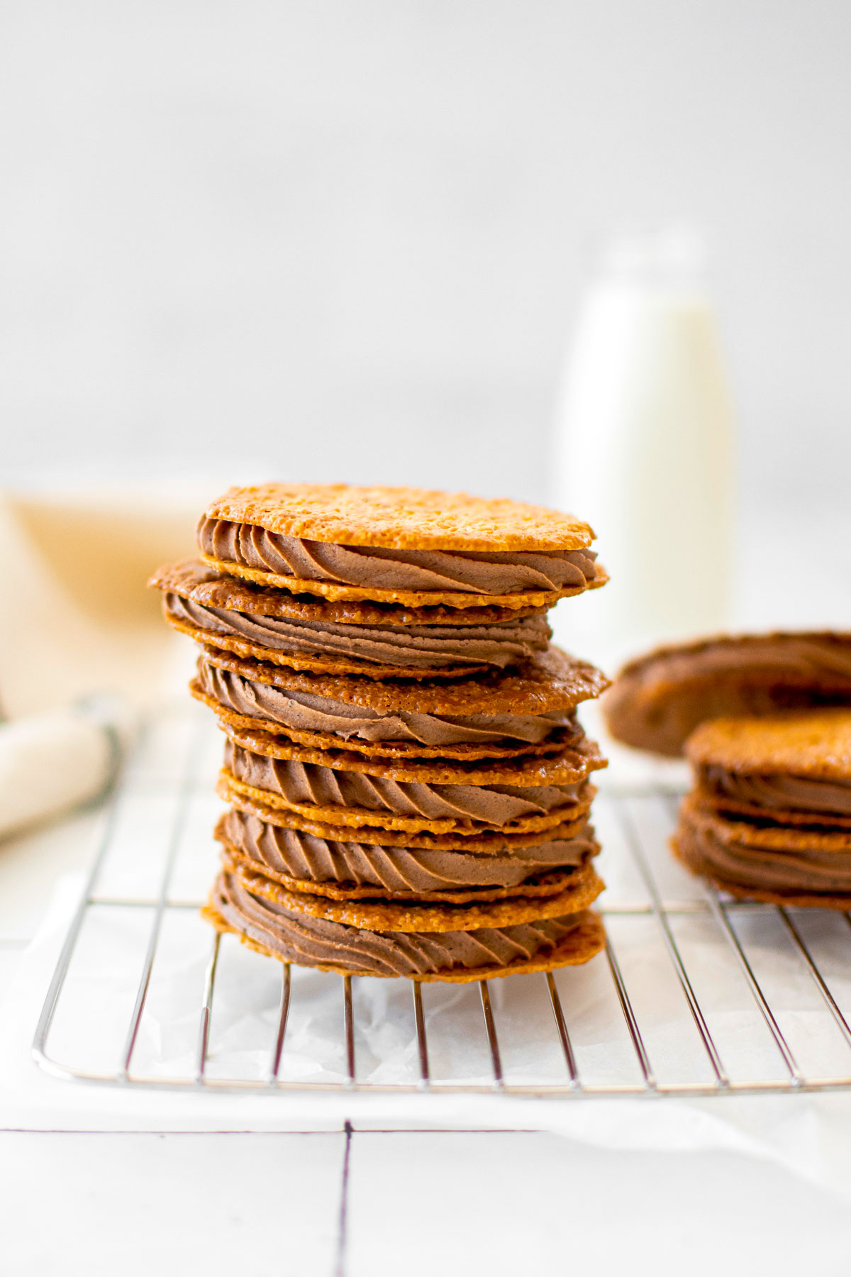 stack of chocolate peanut butter florentine sandwich cookies on a cooling rack on a white tile counter.