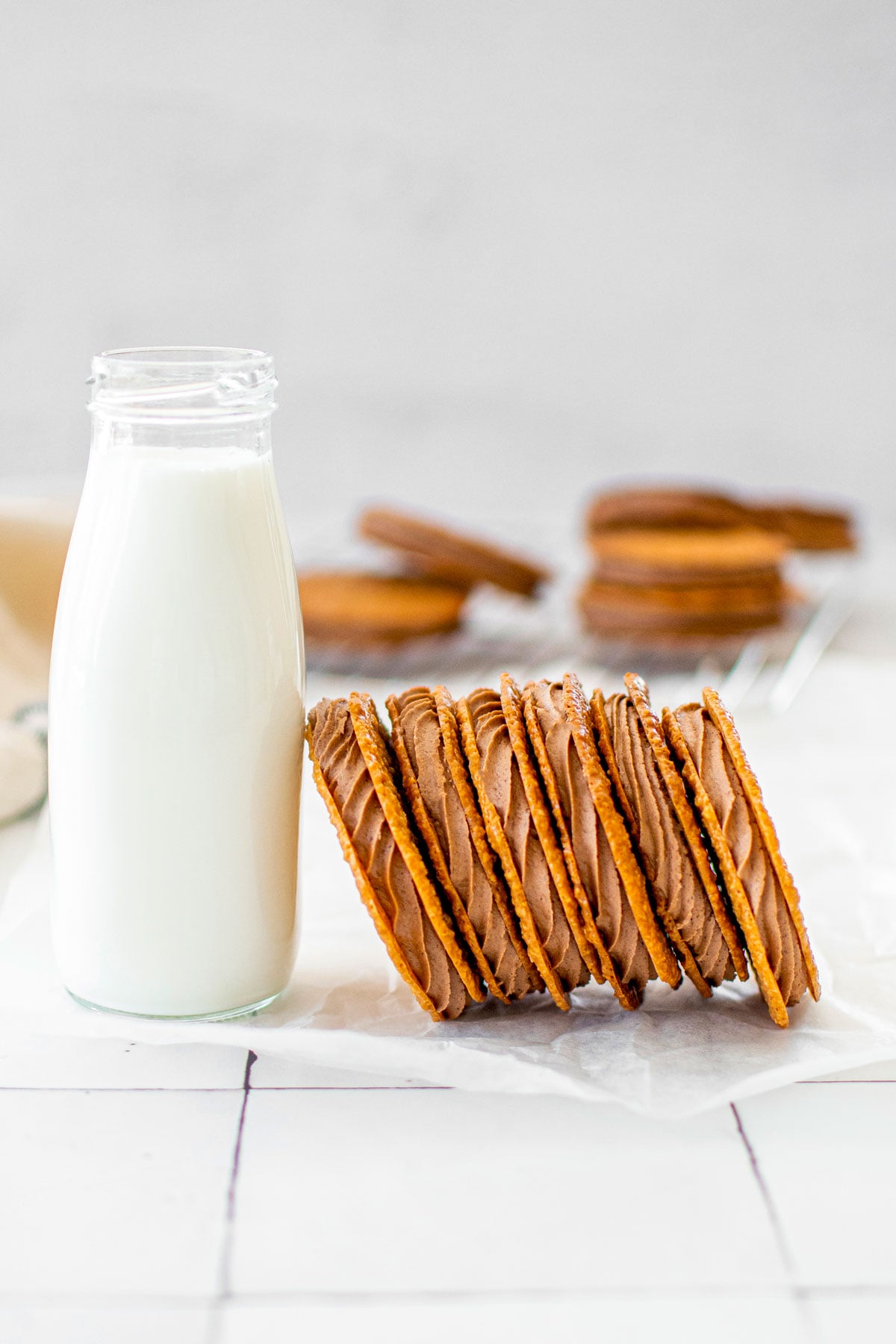 stack of chocolate peanut butter florentine sandwich sandwich cookies with a bottle of milk on a white tile counter.